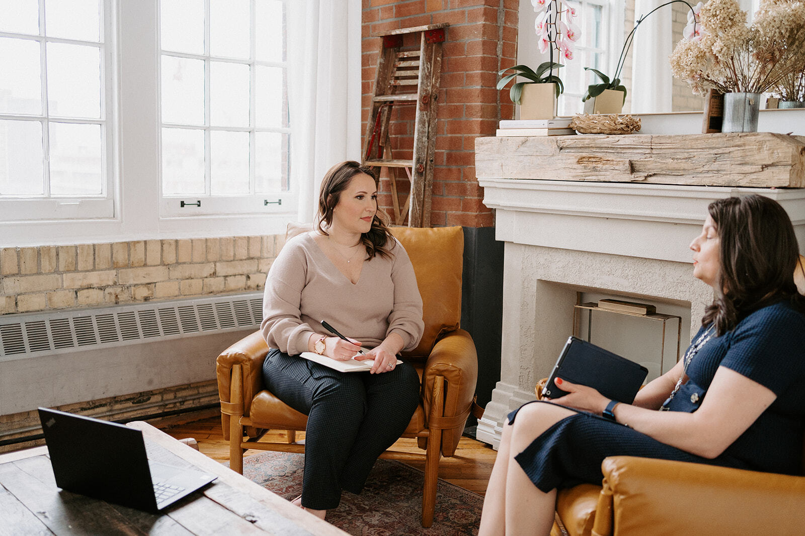 Two women seated and taking notes in silhouette.